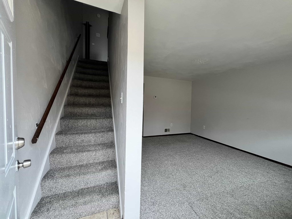A room with a carpeted floor and a staircase with a wooden handrail.