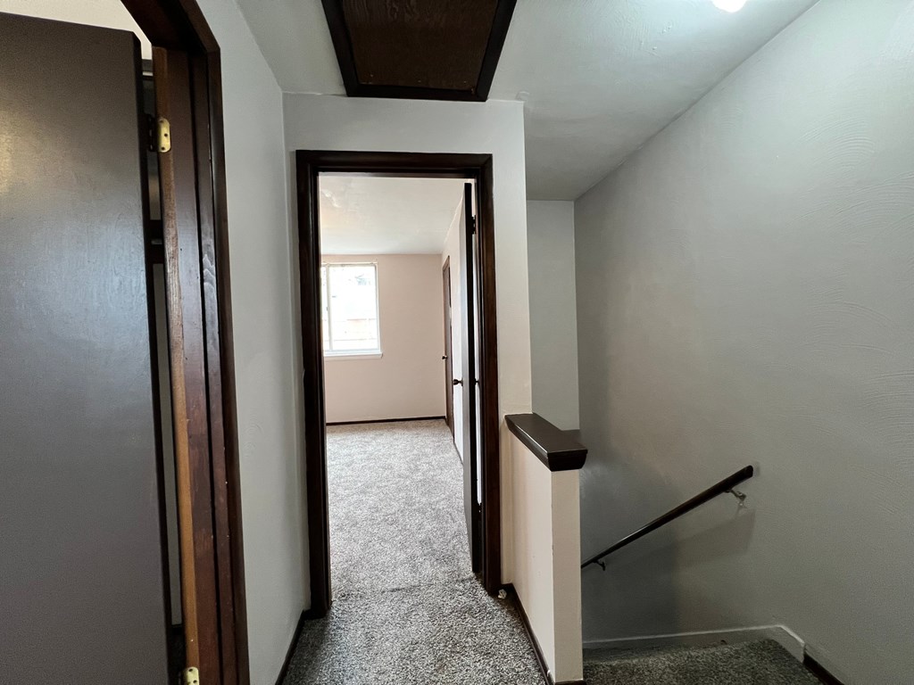 A hallway with a carpeted floor and a staircase with a wooden handrail.