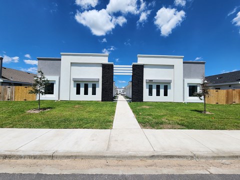 the front of a white house with a sidewalk and grass