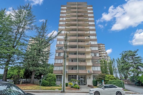 A tall residential building with a parking lot in front.