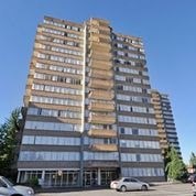 A tall building with many windows and balconies is surrounded by cars.