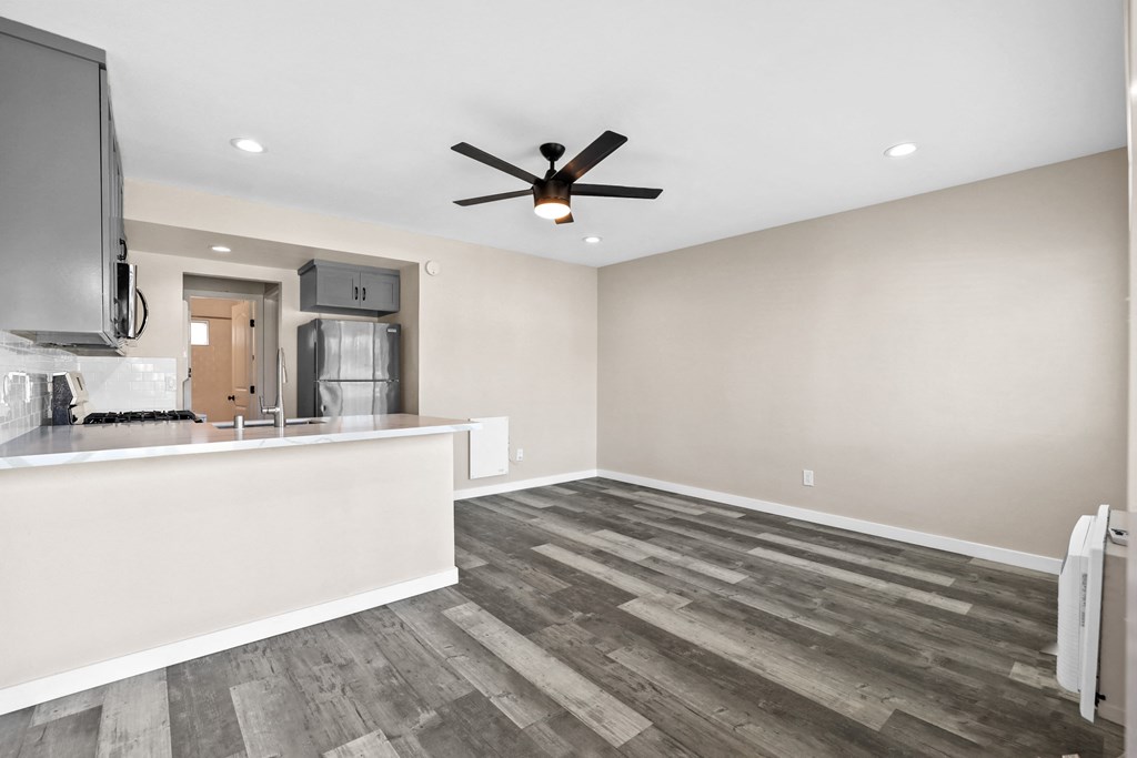 an empty living room with a kitchen and a ceiling fan