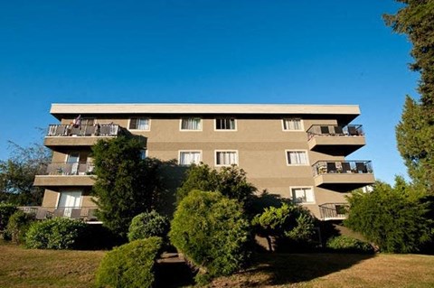 A large building with balconies is surrounded by greenery.