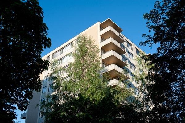 A tall building with balconies is surrounded by trees.