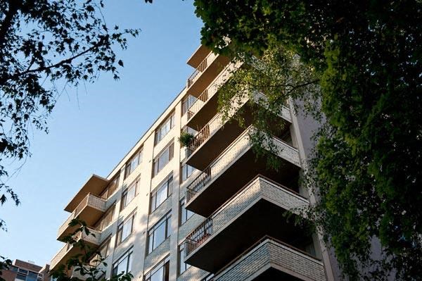 A tall building with balconies is surrounded by trees.