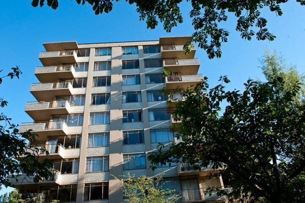 A tall building with balconies is surrounded by trees.