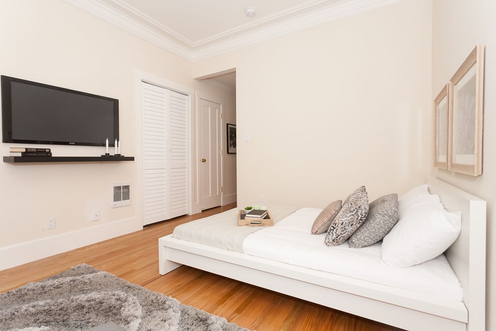 A white bed with a grey rug in front of it.