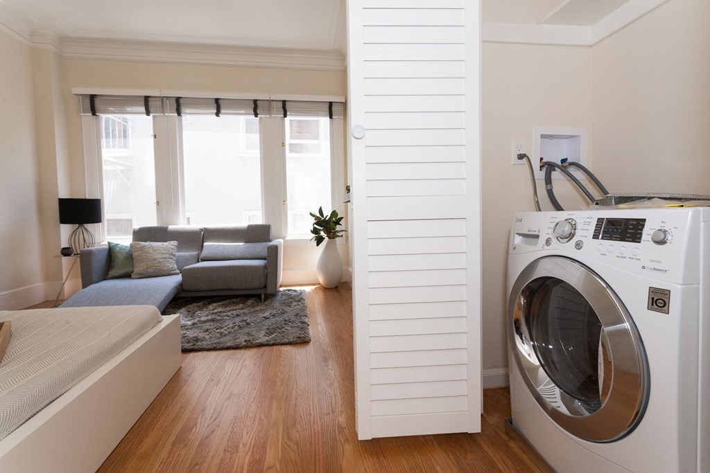 A modern laundry room with a washing machine and a bedroom with a couch and a window.