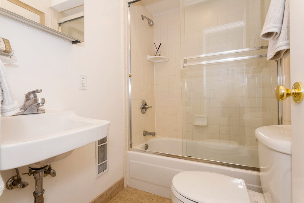 A white sink with a gold faucet is on the left of a white toilet in a bathroom.