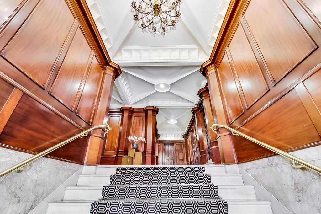 A staircase with a black and white carpeted runner leads up to a chandelier.