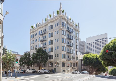 A large building with many windows and balconies is in the middle of a city street.