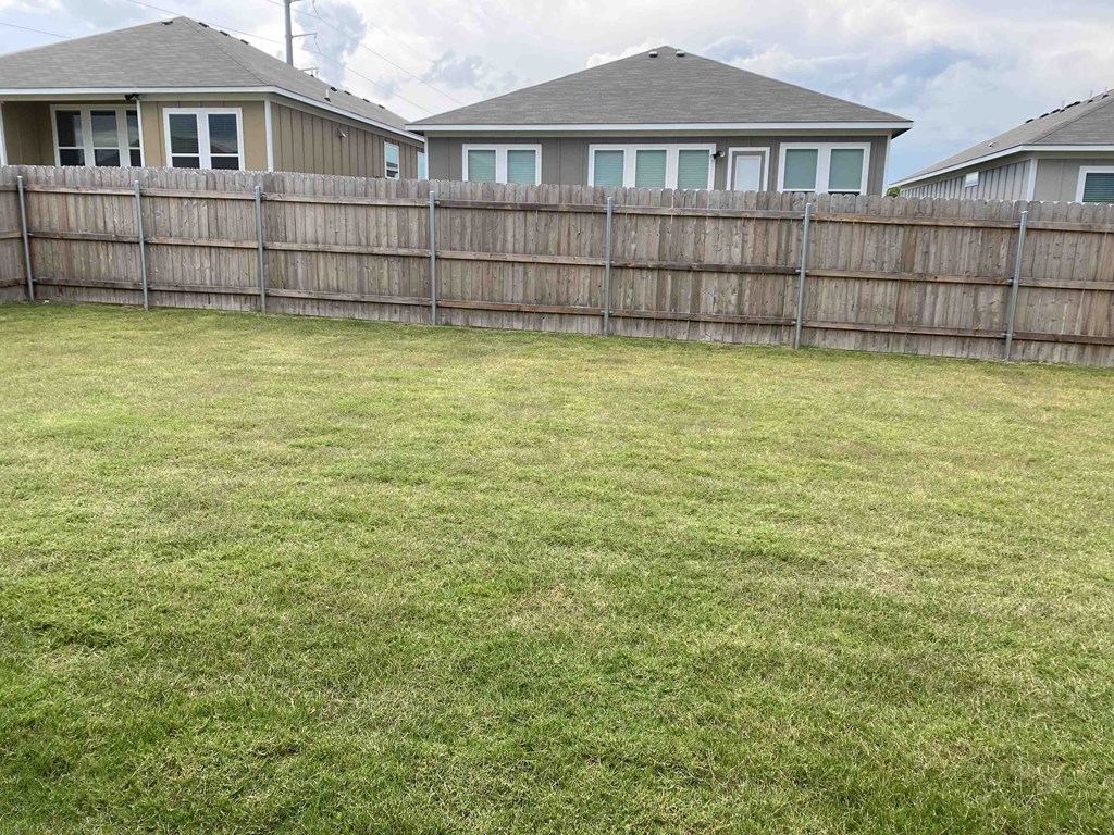 a backyard with a fence and a house in the background