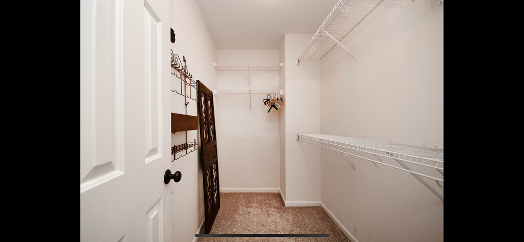 a walk in closet with white walls and shelves and a white door