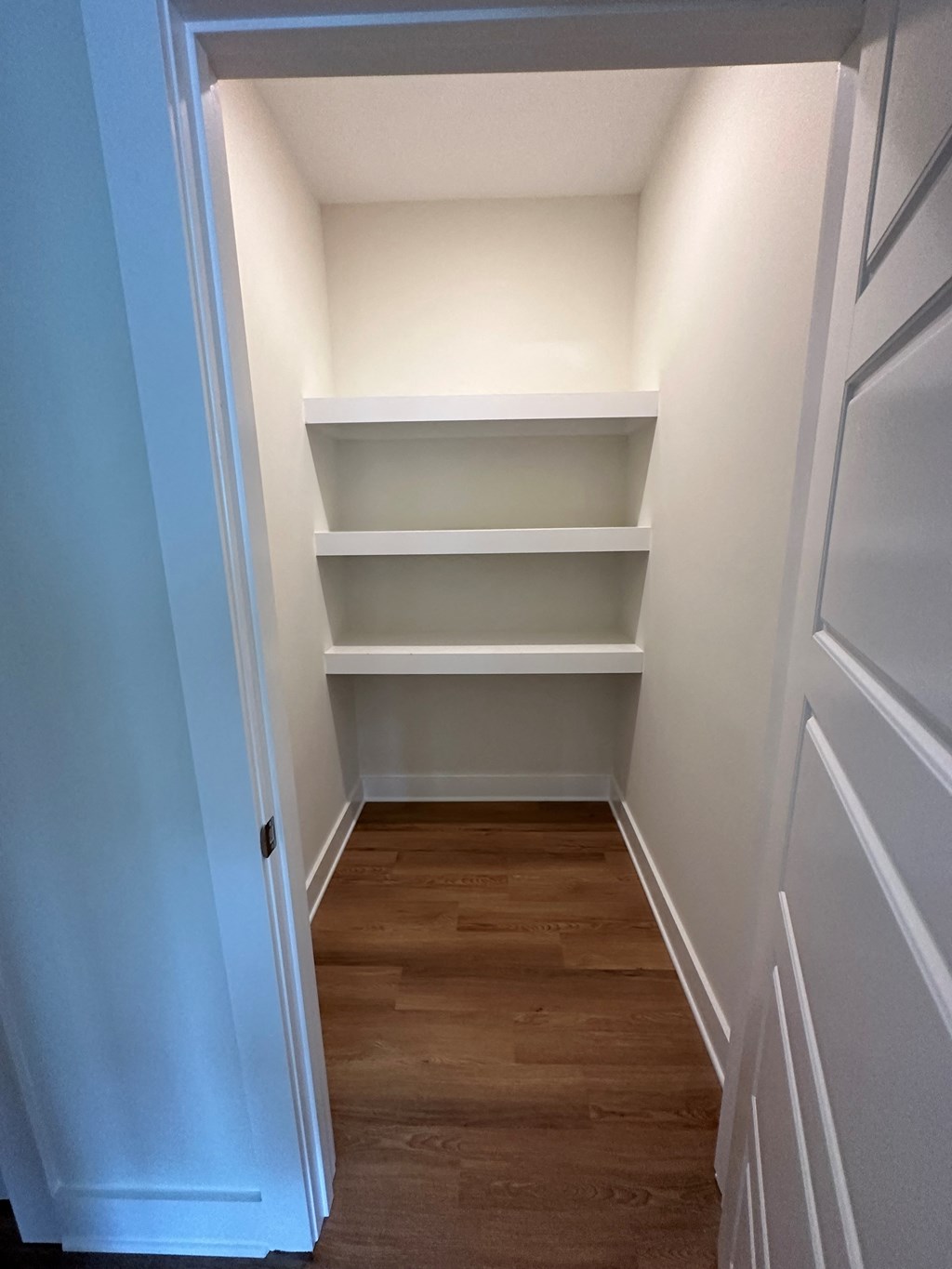 a walk in closet with white shelves and a wood floor