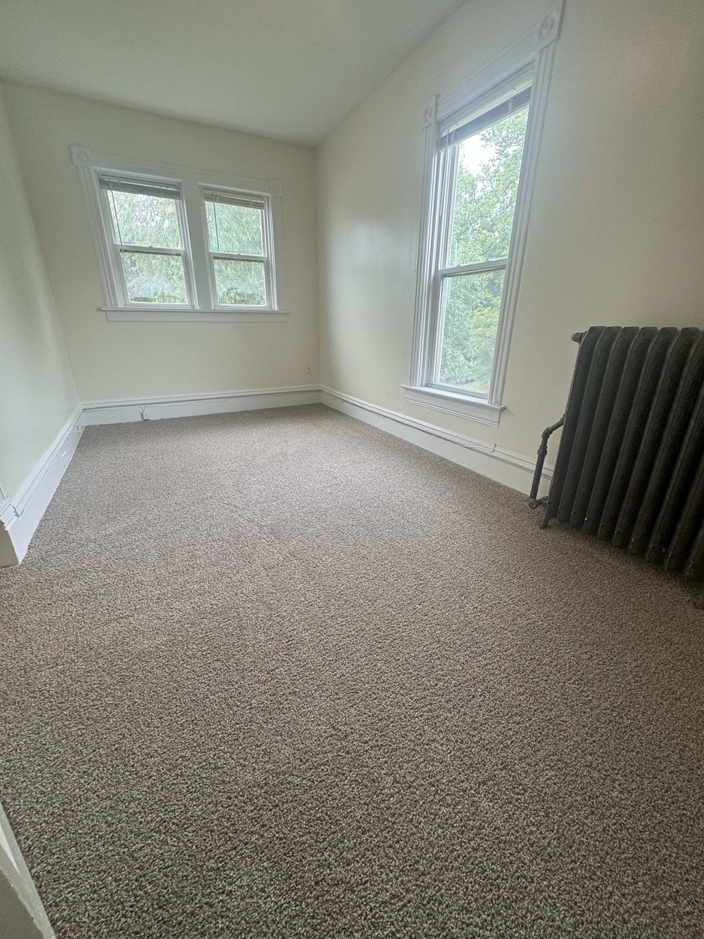 A room with carpeted floor and two windows.