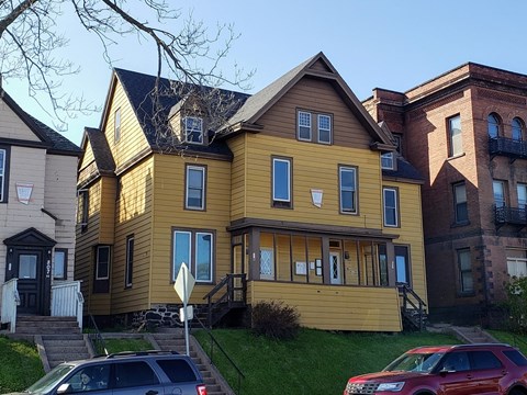 a yellow house with a yard and cars parked in front of it