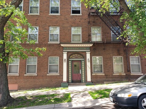 A brick building with a red door and a tree in front.
