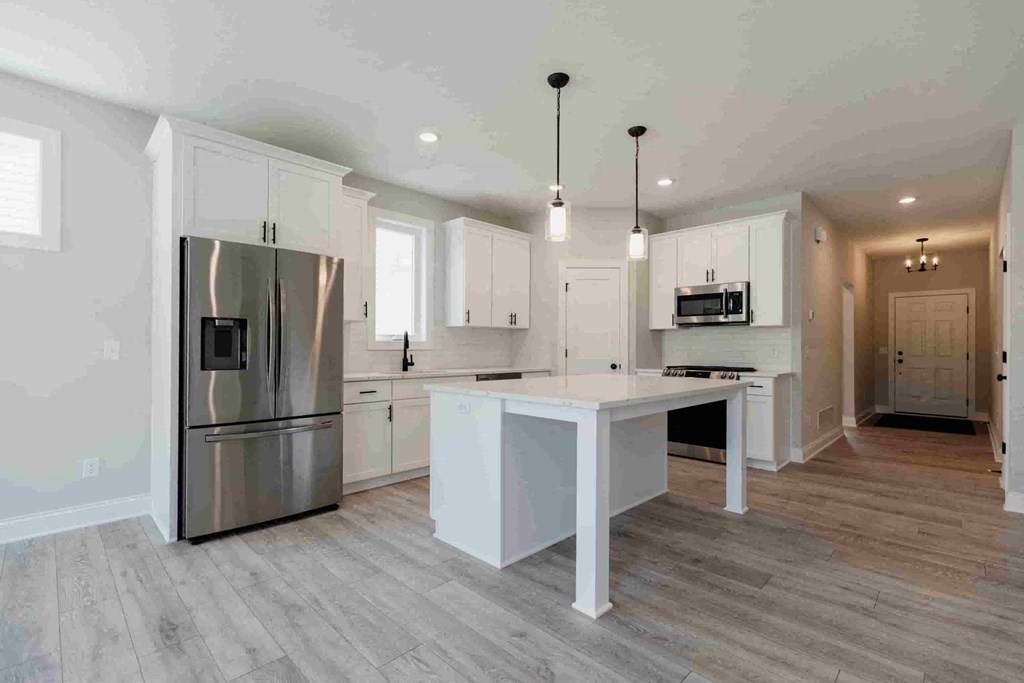 a white kitchen with a large island and stainless steel refrigerator