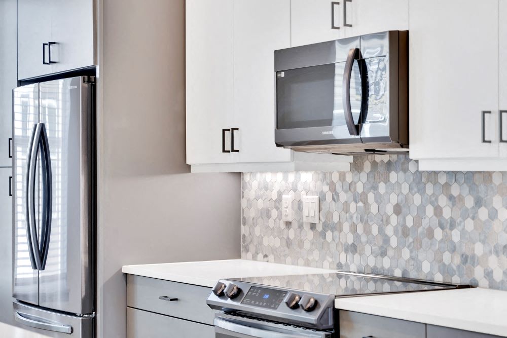 Close up view of kitchen with tile backsplash, under cabinet lighting, soft closing cabinets and black stainless steel appliances