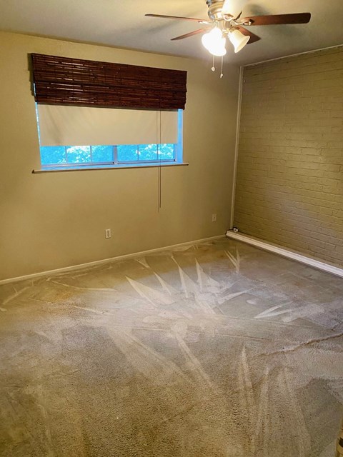 a room with a carpeted floor and a window and a ceiling fan