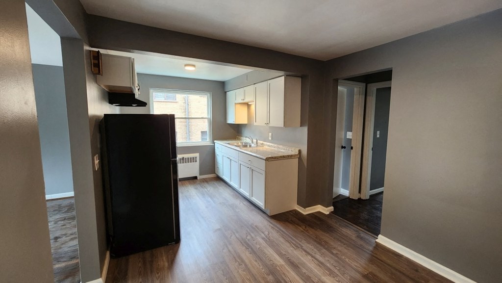 an empty living room and kitchen with hard wood floors and white cabinets