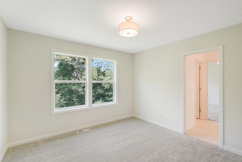 an empty bedroom with two windows and a door to a hallway