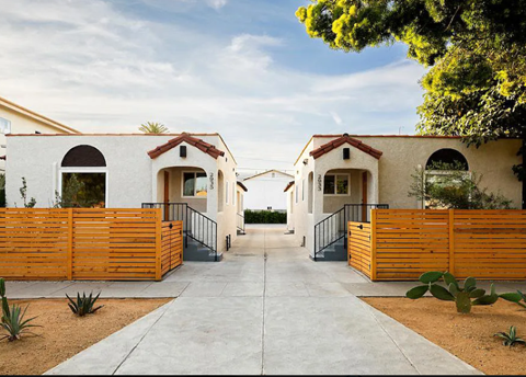 A row of houses with wooden fences and cacti in front.