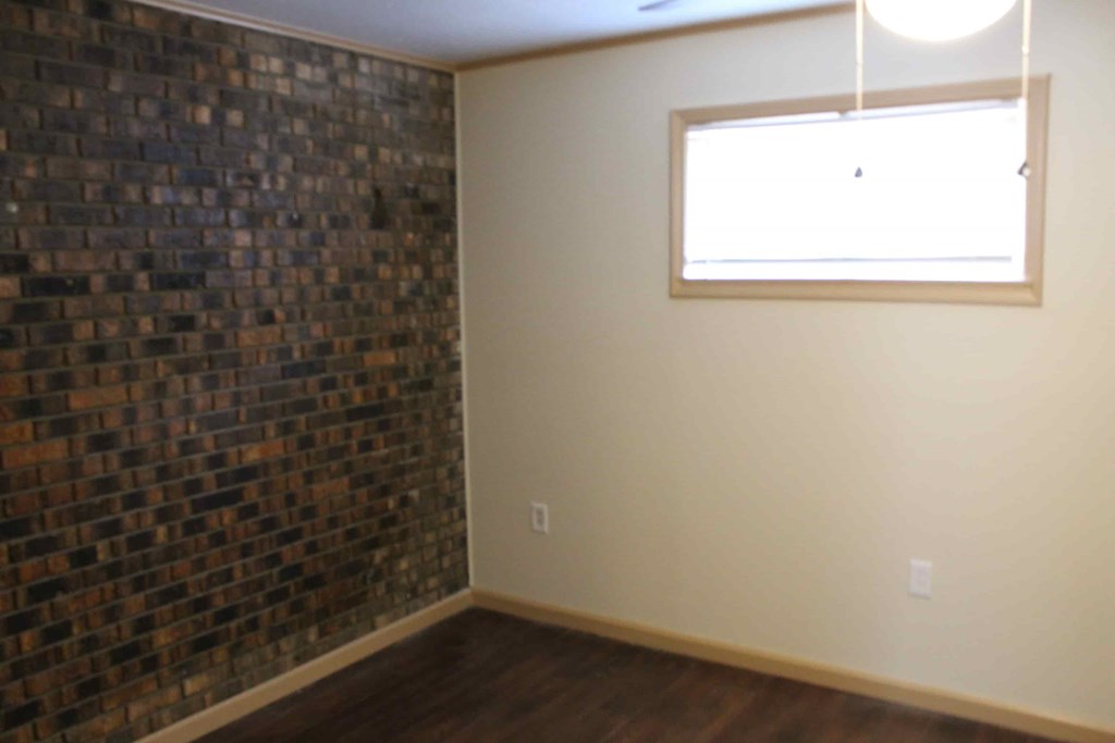 an empty living room with a window and a brick wall