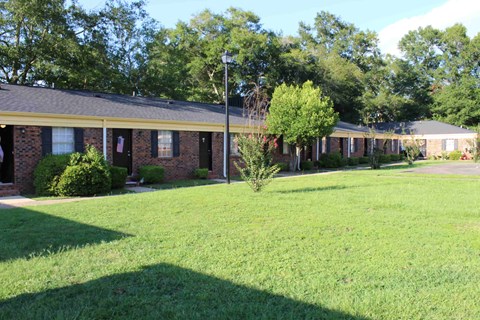 the front of a brick house with a lawn and trees
