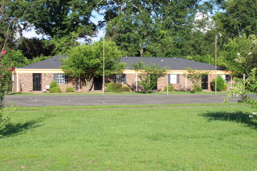 the front of a brick house with a lawn and trees