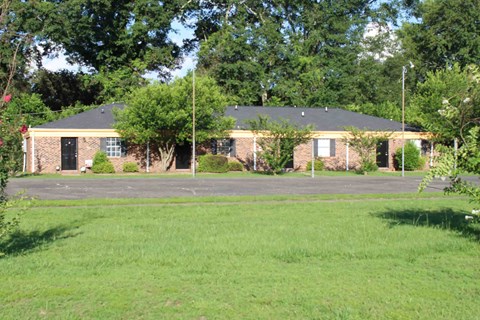 the front of a brick house with a lawn and trees