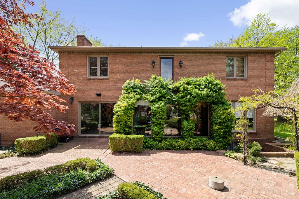 the front of a brick house with a brick patio and hedges