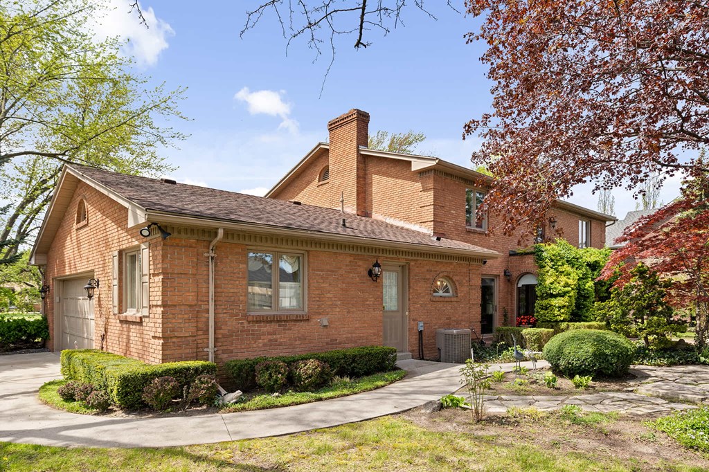the front of a brick house with a sidewalk and a tree