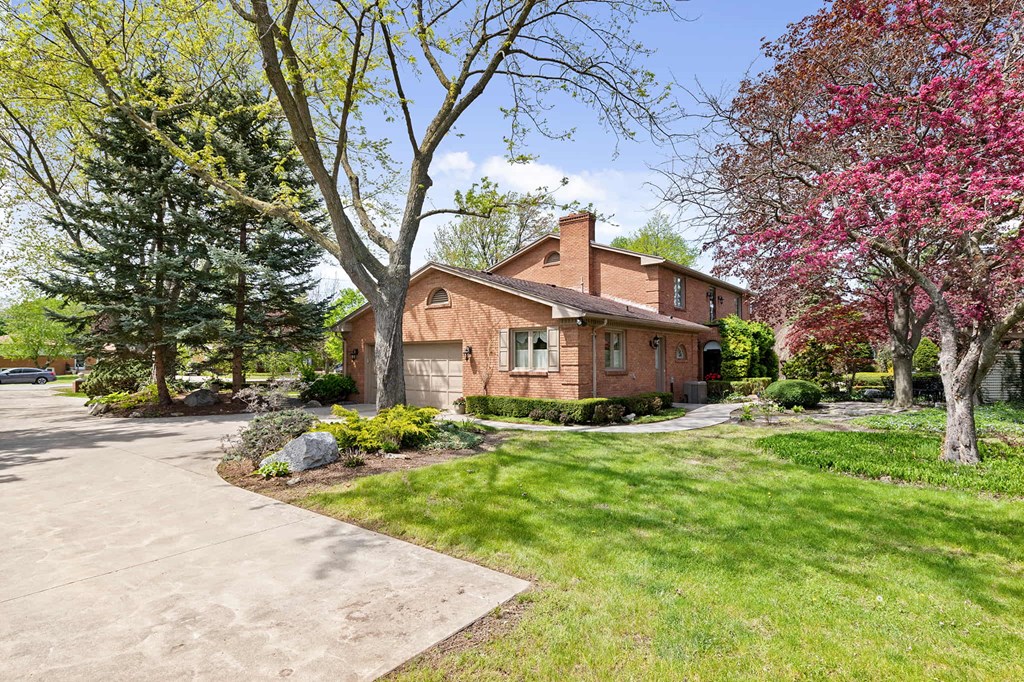 the front of a brick house with a driveway and trees