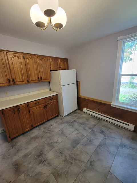 an empty kitchen with a refrigerator and wooden cabinets