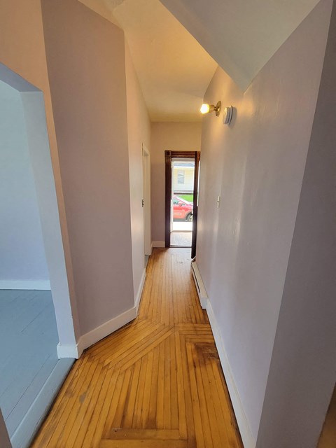 a hallway with white walls and wooden floors and a door to a house