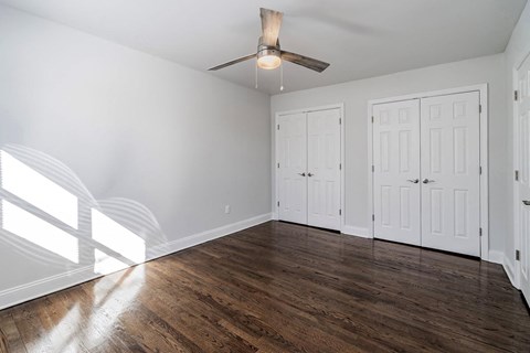 an empty living room with a ceiling fan and white closets