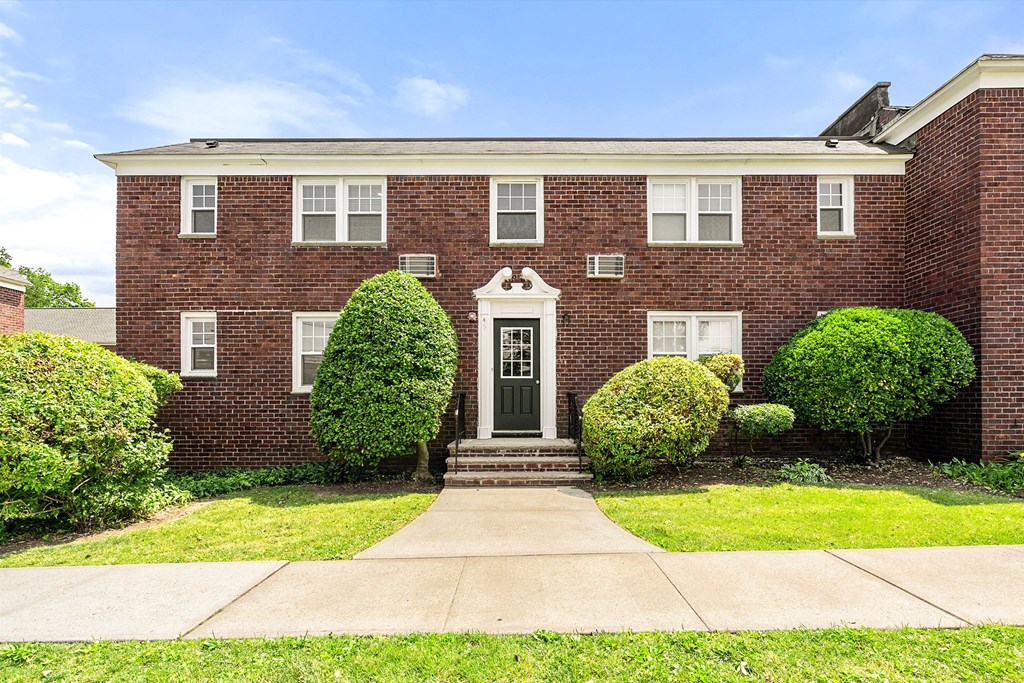 a red brick house with a green lawn and a sidewalk in front of it
