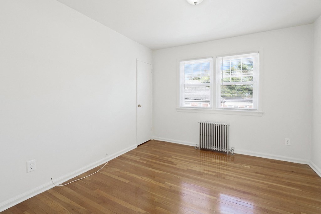 a bedroom with white walls and wood floors and a radiator