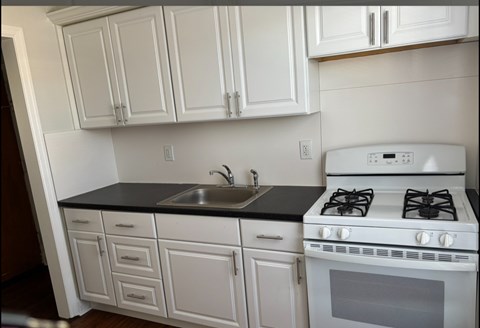A white kitchen with a black counter top and a white stove.