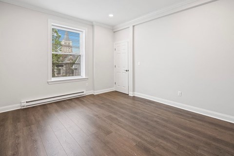 A room with a wooden floor and a window showing a building outside.