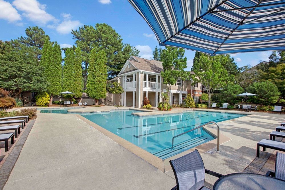 a large pool with chairs and umbrellas next to a house