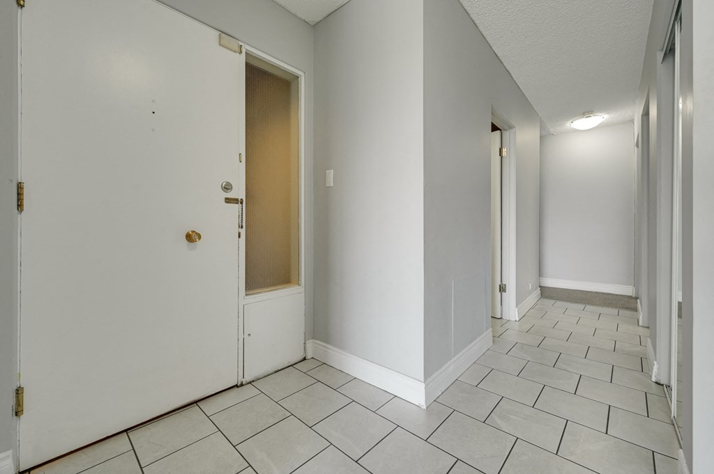 the living room and entryway of a house with white walls and tiled floors