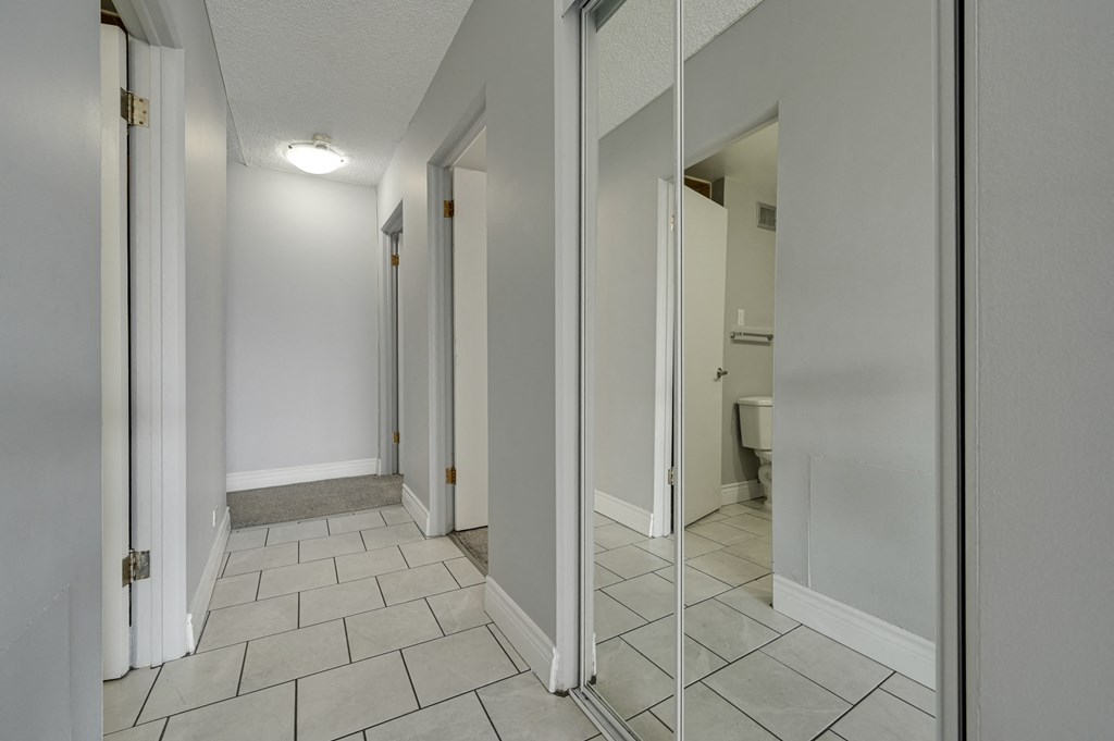 an empty hallway with mirrored doors and a bathroom in the background