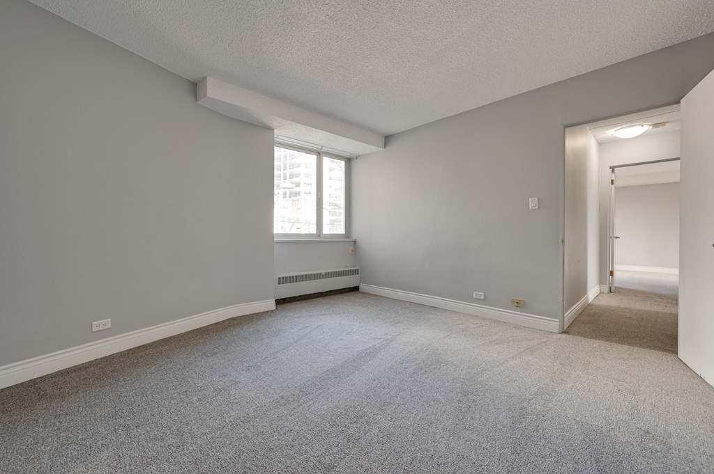 the living room and dining room of an apartment with carpeting and a window