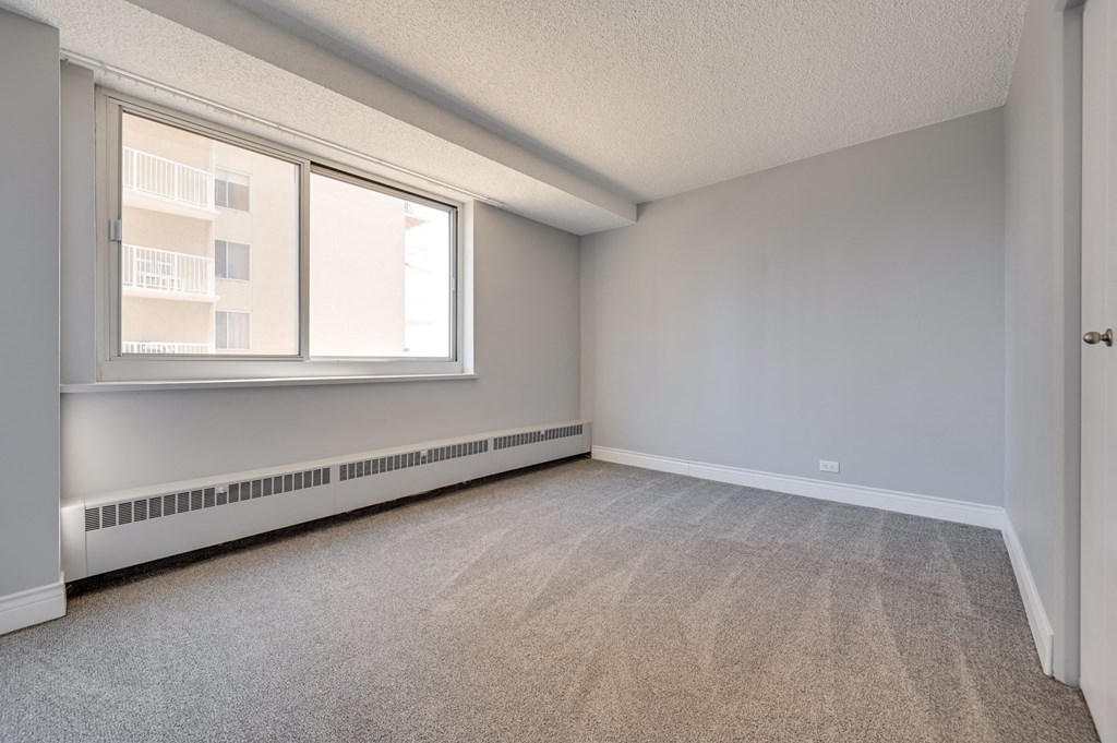 an empty bedroom with a large window and carpeted flooring