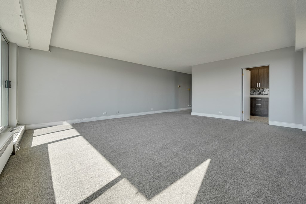 an empty living room with carpet and a door to a bathroom