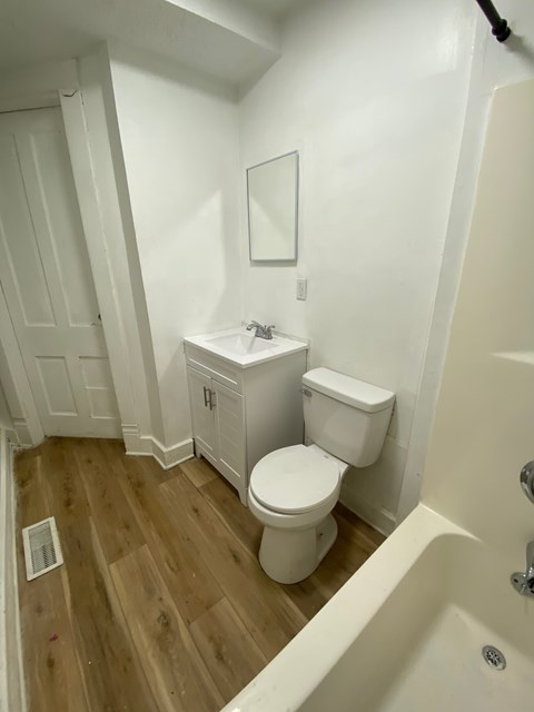 A white toilet sits in a bathroom next to a bathtub.