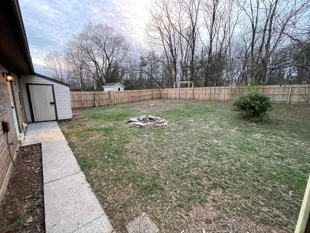 a backyard with a fence and a fire pit in the grass