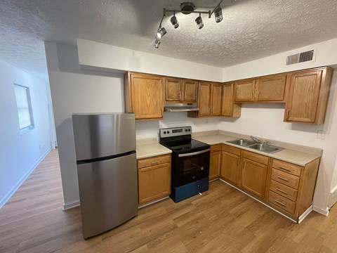 an empty kitchen with wooden cabinets and a stainless steel refrigerator